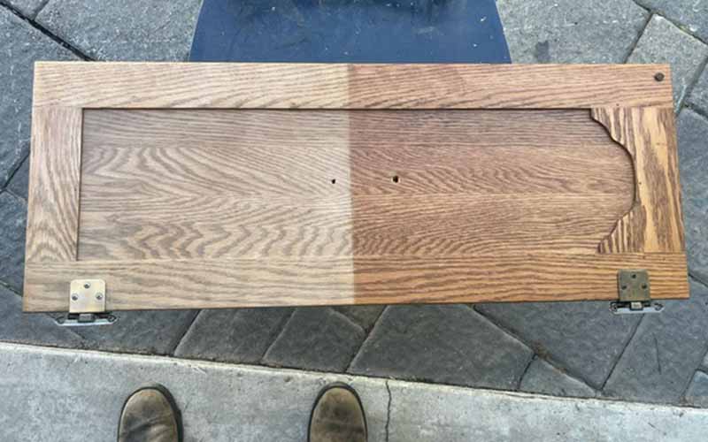 A wooden cupboard door, half of which has had its varnish removed by a laser cleaning machine