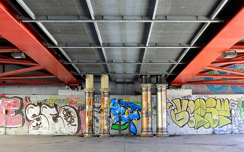 A photo of a wall of graffiti underneath a steel bridge