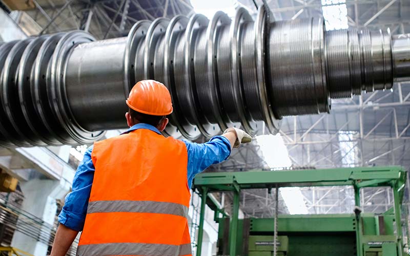 A man in a hard hat and safety vest works with large machinery in a factory