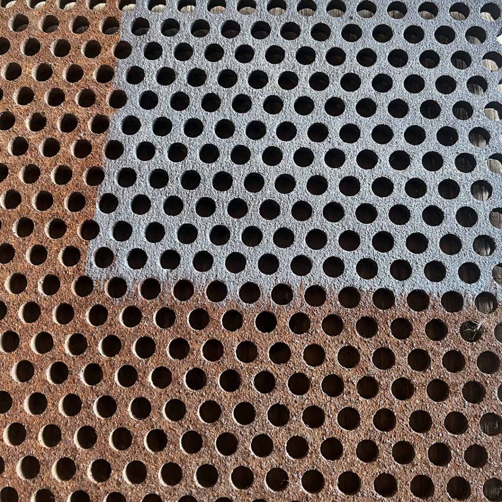 Closeup shot of a piece of metal with circular holes; part of the metal has been laser cleaned and is silver coloured while the rest is rusty